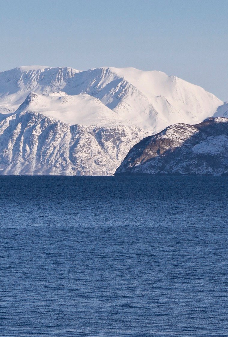 Snødekte fjell over den blå Kvænangsfjorden en klar vinterdag